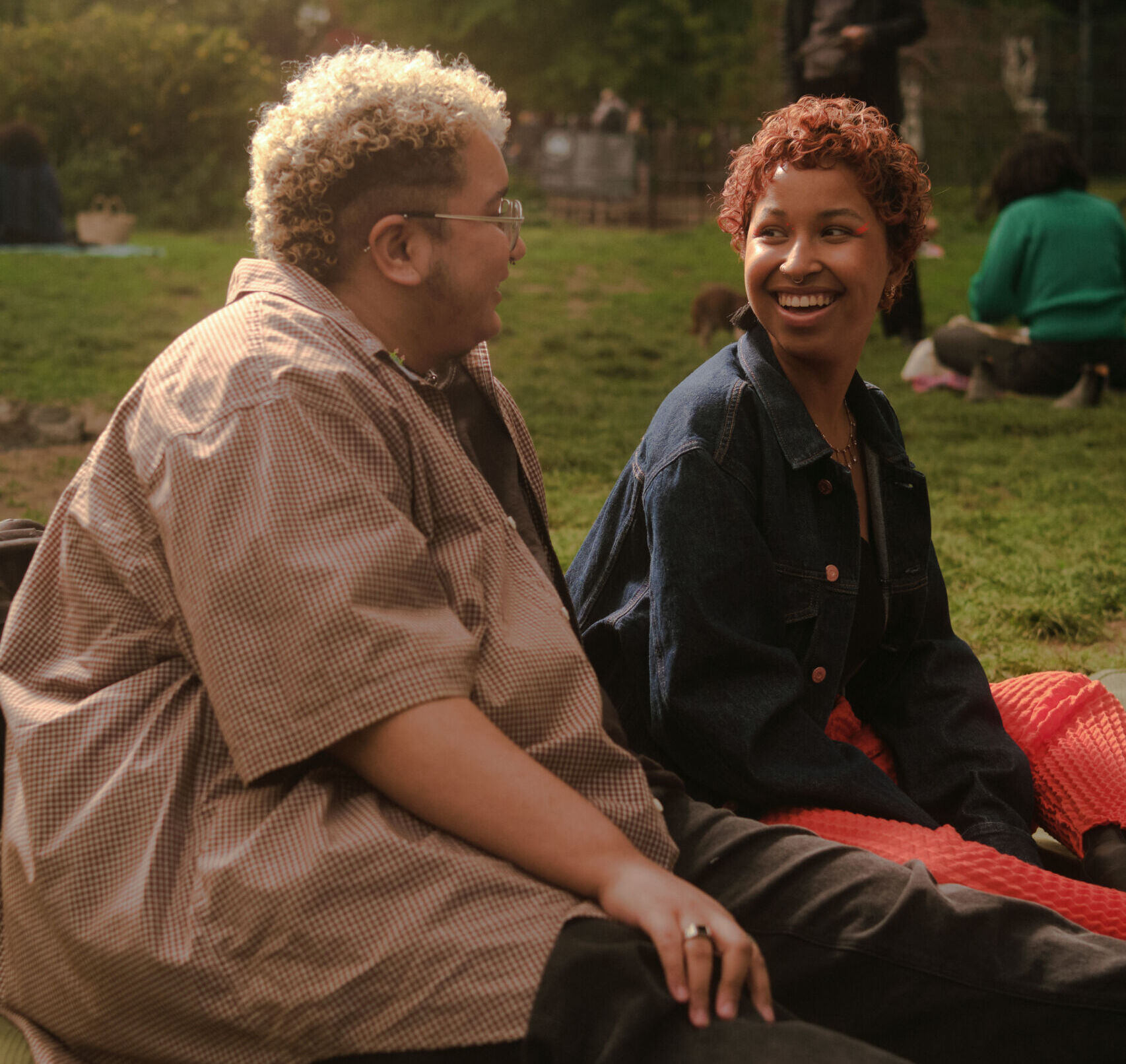 Two trans folx sit together in a park